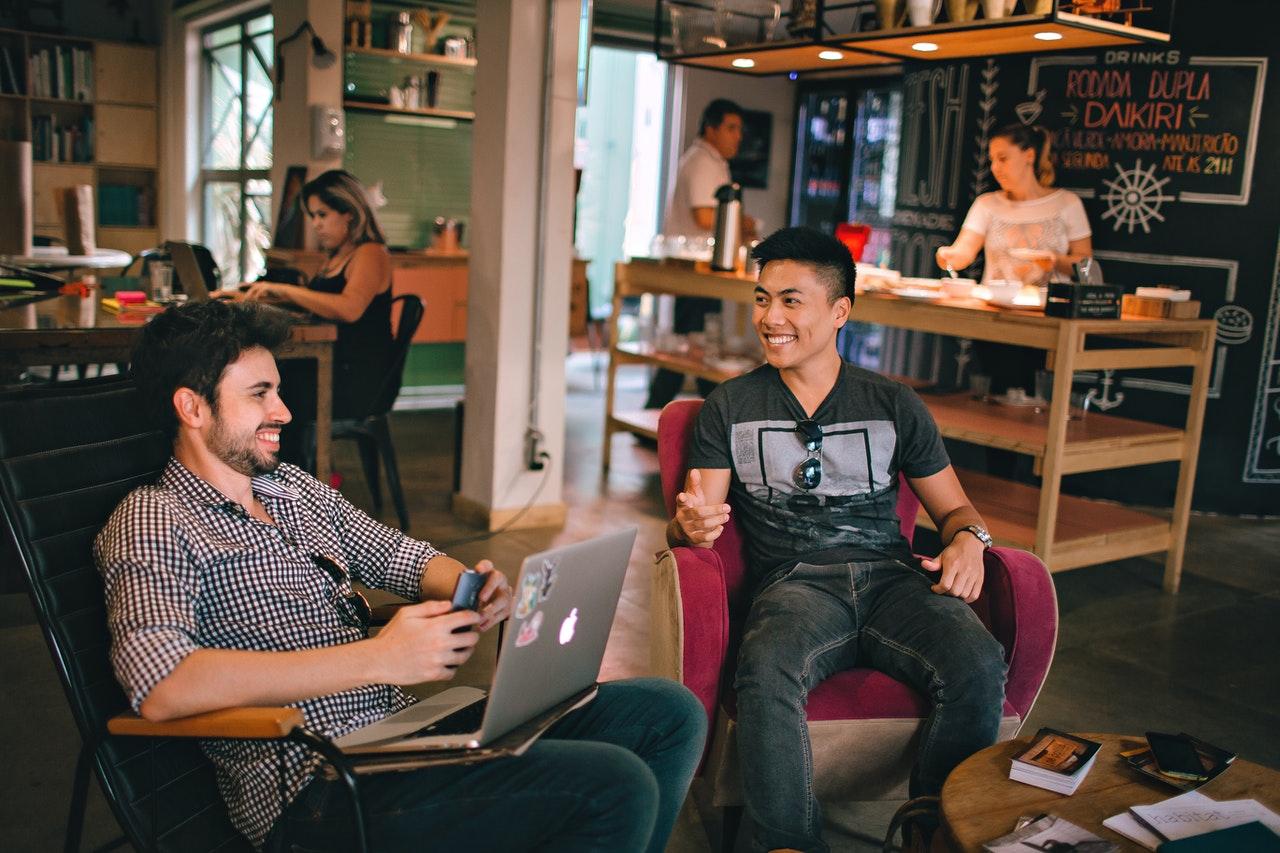 Two male friends talking and smiling while sitting in a coffee shop where they have gone to socialise