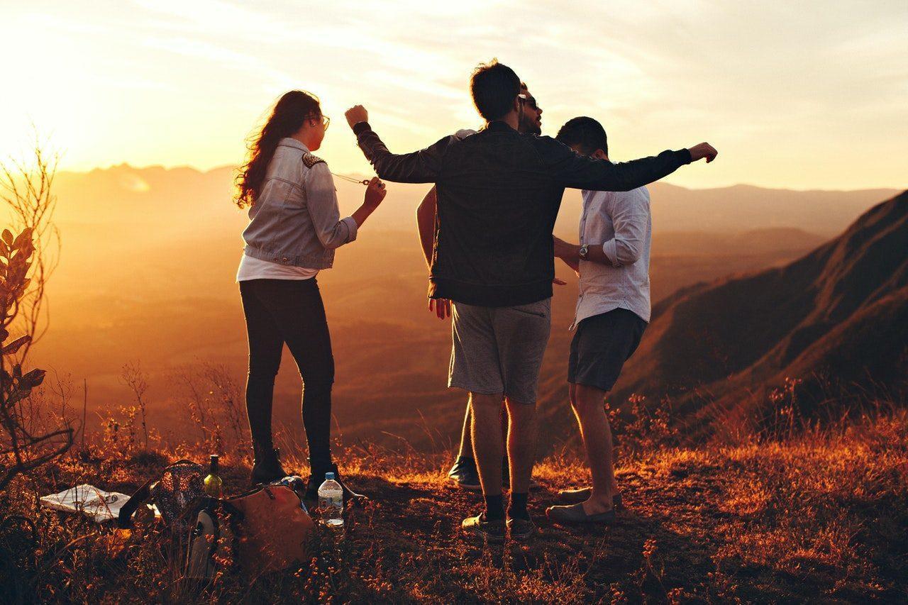 Four friends dancing at the top of a hill that they have hiked to so they can socialise