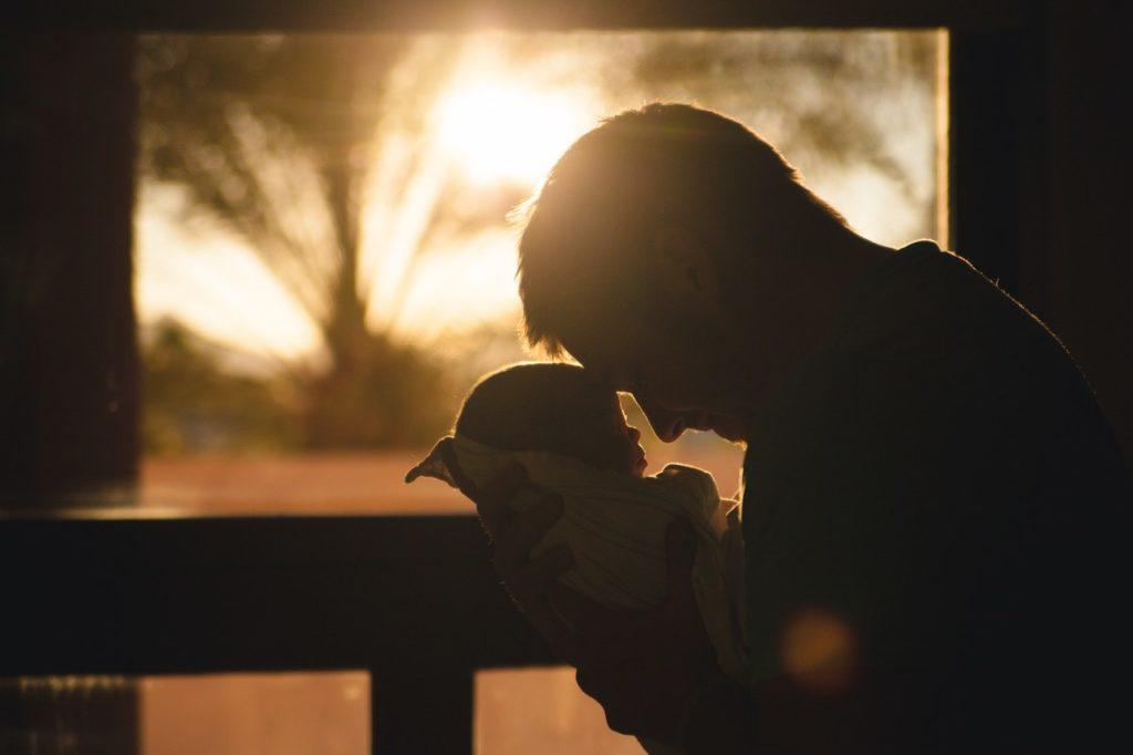 Father holding baby and touching heads as they socialise and bond in front of a sunrise