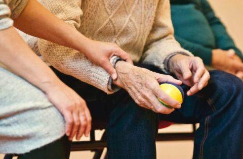 A volunteer woman holding an elderly man's wrist to support him