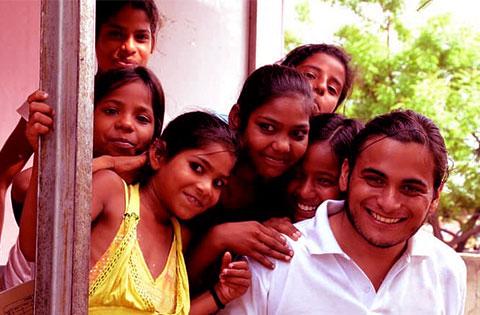 A volunteer surrounded by smiling girls as he helps them