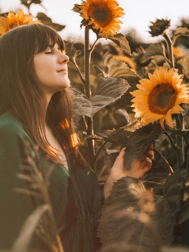 Lady breathing in deeply and peacefully in a field of tall sunflowers, boosting her well-being