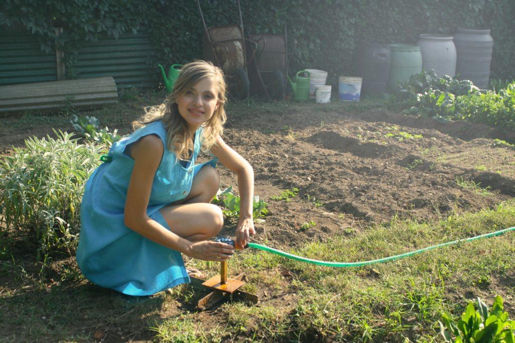 Woman Holding Green Garden Hose amongst prepared beds in the Fresh Air