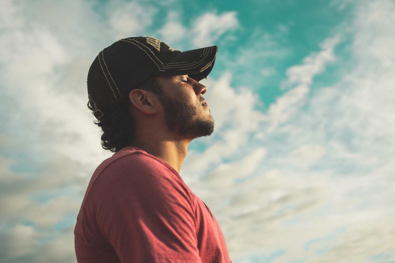 Man Wearing Black Cap With Eyes Closed Under Cloudy Sky breathing deeply feeling prepared and relaxed