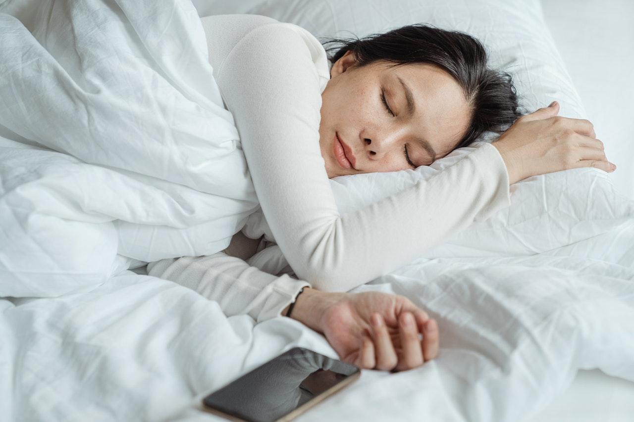 Lady lying on a bed next to a mobile phone in light sleep