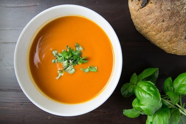 Bowl of soup next to some fresh bread and some basil