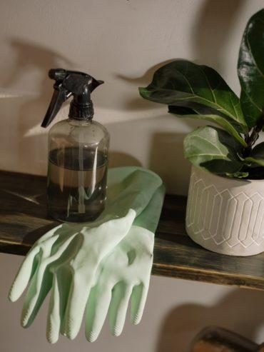 Green rubber gloves and a spray bottle on a shelf, ready for use, as cleaning boosts well-being