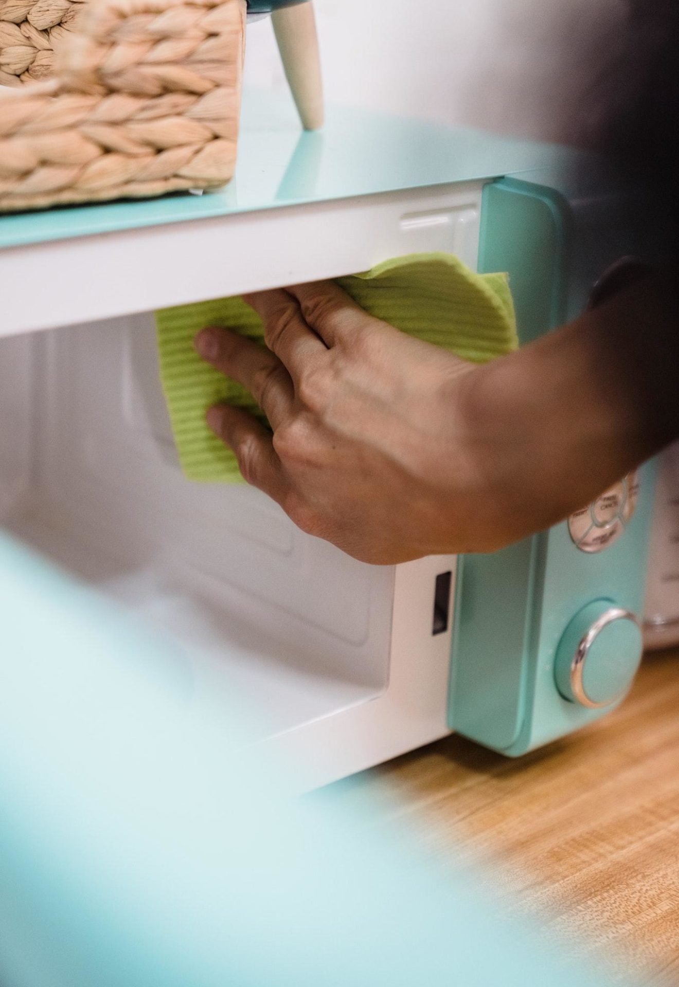 Person cleaning the inside of a microwave with a green cloth