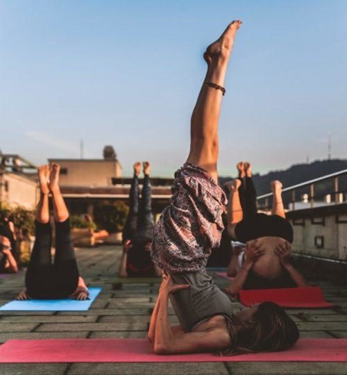 Group of people doing yoga, lying on backs with legs in the air while supporting their backs