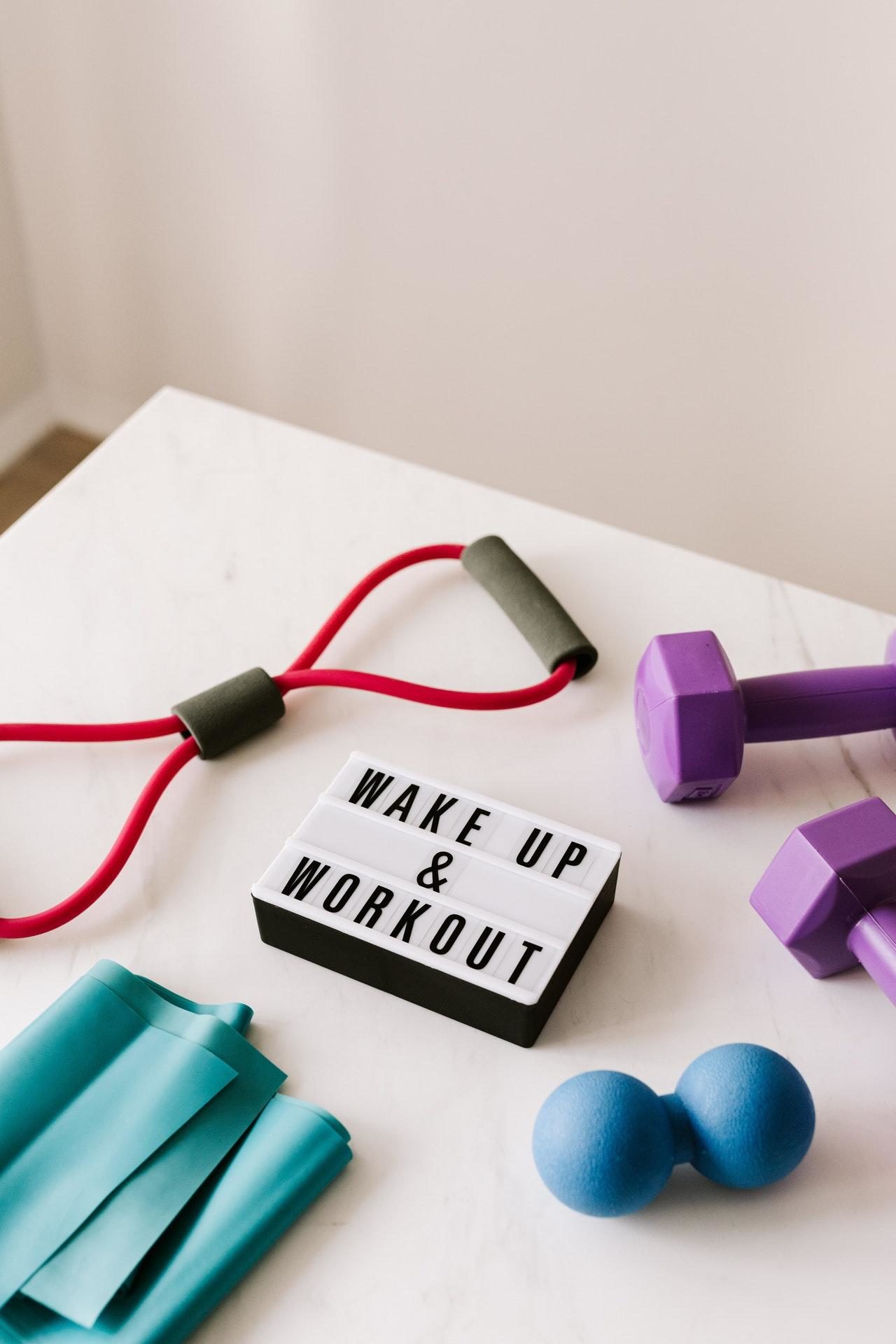 The words "Wake up and work out" in black and white next to dumbells, weights and a stretch band