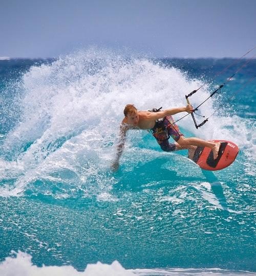 Man kite-surfing on an orange board in blue water