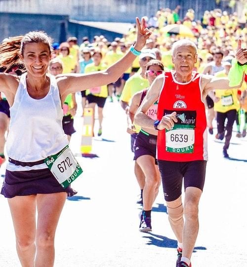 Female and male runners doing the Douro marathon and smiling. The lady showing the peace sign and the man with thumbs up