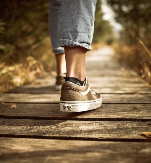 Feet and legs to knees of person walking on boardwalks next to greenery