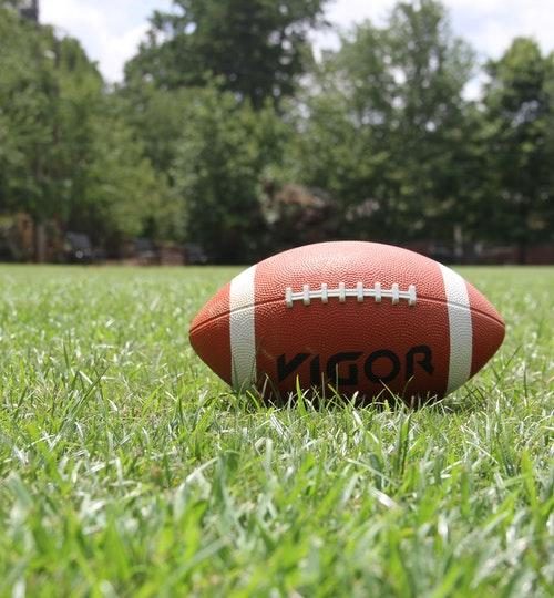 Rugby ball on green grass next to trees