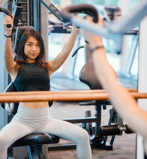 Woman in Black Sleeveless Crop-top and White Leggings Using a Butterfly Machine in Front of a Mirror