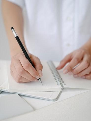 A person writing into a notebook boosting their well-being by prioritising and taking control