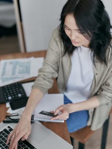 Lady tapping her credit card details into her laptop as she works through her bills and keeps on top of her Life Admin list, boosting her well-being