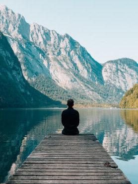 Man sitting at the end of a boardwalk looking over a lake and mountains contemplating his well-being in the Fresh Air