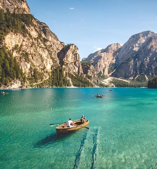 People rowing across clear turquoise water between mountains